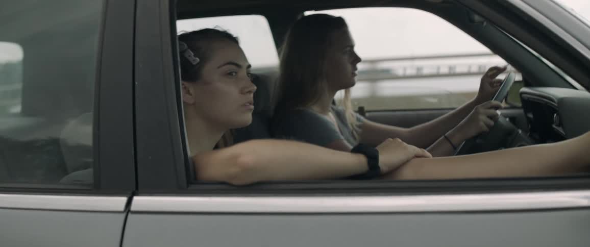 Two women ride in a car while the driver smokes a cigarette