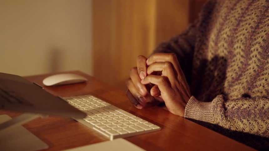 Man sits at a table in front of a computer moving his hands near the keyboard