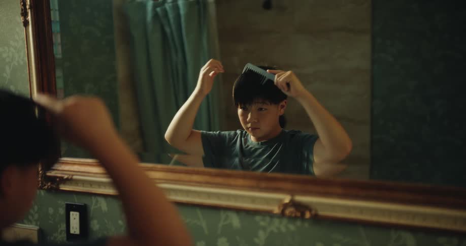 The boy is brushing his hair in the mirror