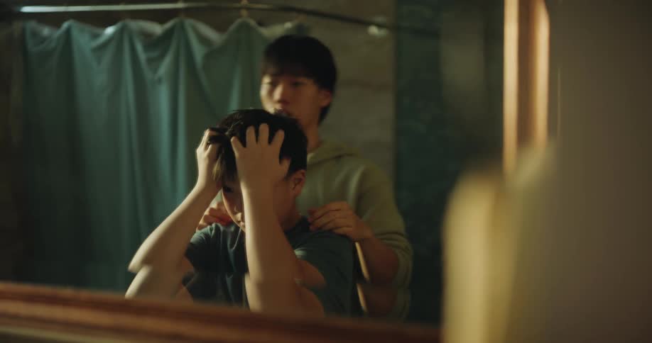A teenage boy styling a younger childs hair as they both look into a mirror