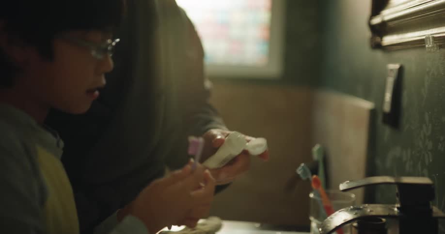 Adult asian man teaching a young asian boy to brush his teeth in a bathroom indoors during day time