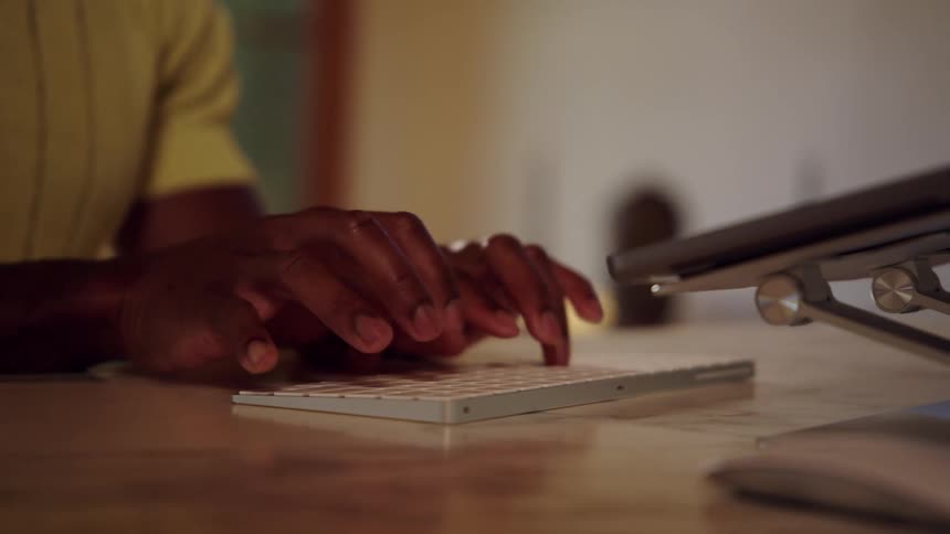 Hands type on white keyboard over light desk in softly lit indoor setting