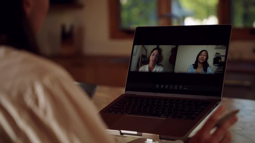 Person attends a video call on a laptop displaying two participants on the screen