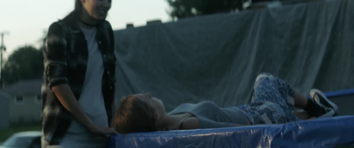 A woman lays on a covered table outside as another woman stands by her and smiles