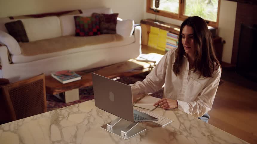 Woman works on a laptop placed on a stand on a countertop in a home setting