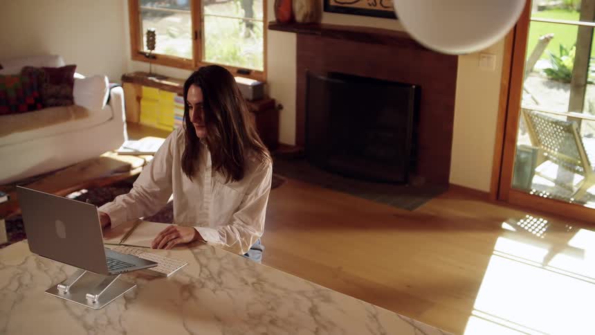 Woman working remotely from home makes notes during a video call