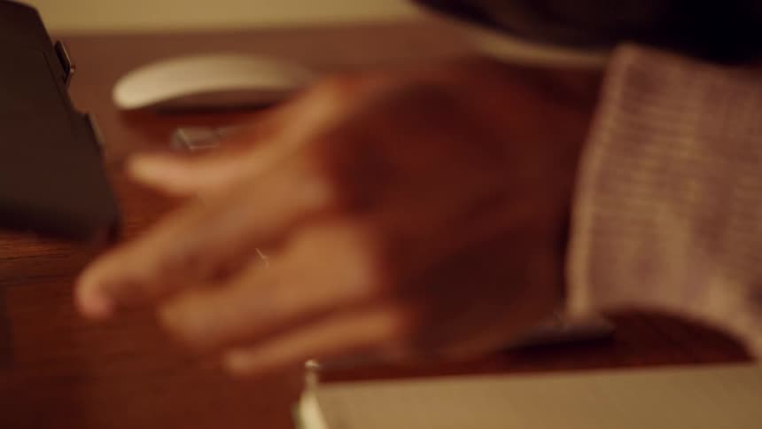 A person sitting at a desk typing on a computer keyboard while holding a mouse