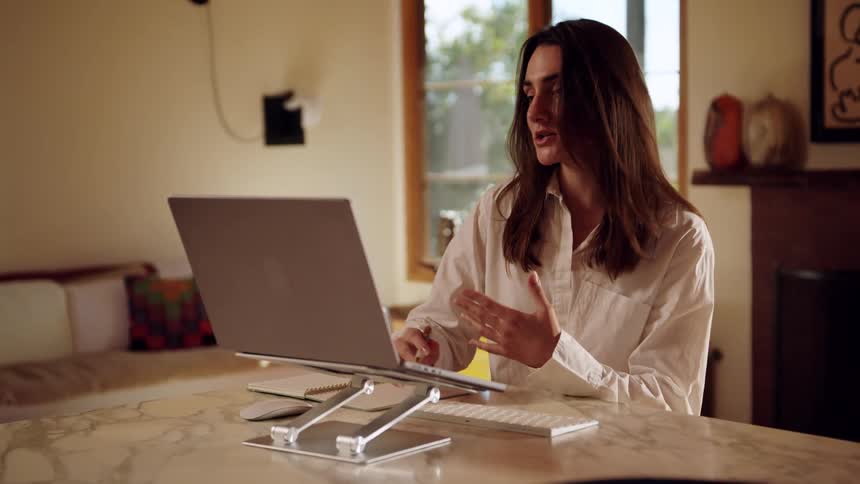 Person works at marble table with elevated laptop and notebook beside