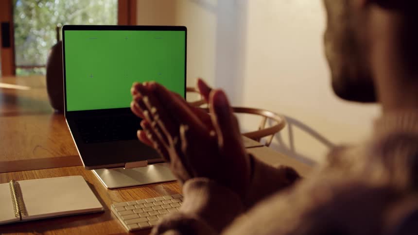 A black man is talking while staring at a green screen on his laptop