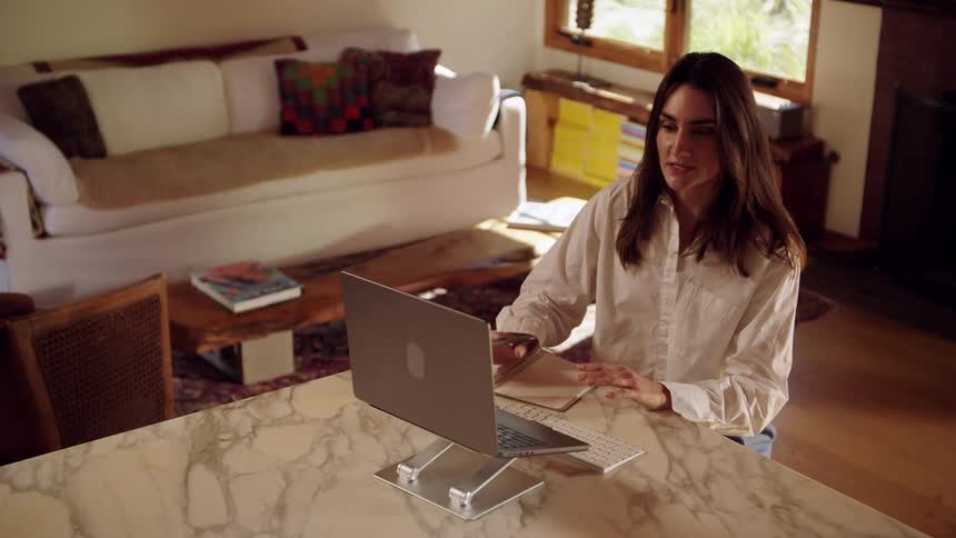 Woman speaks during an online meeting using a laptop placed on a stand in a home setting