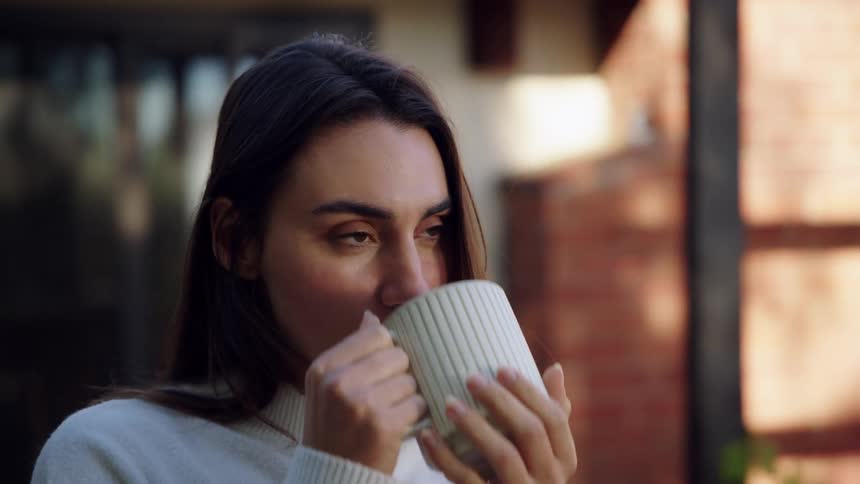 Woman drinking from a mug in an outdoor setting with a blurred residential background