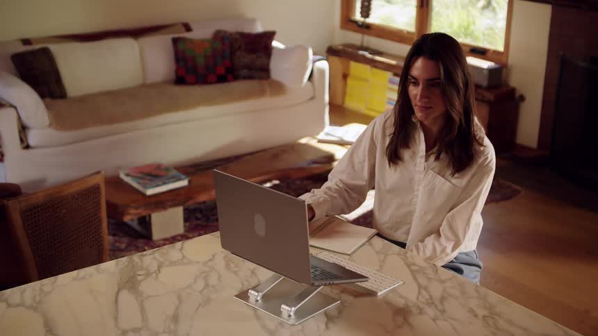 The woman is talking on her laptop while writing