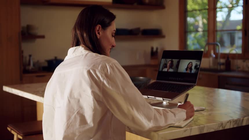 A woman seated in front of a dining table while talking to people in a laptop interview