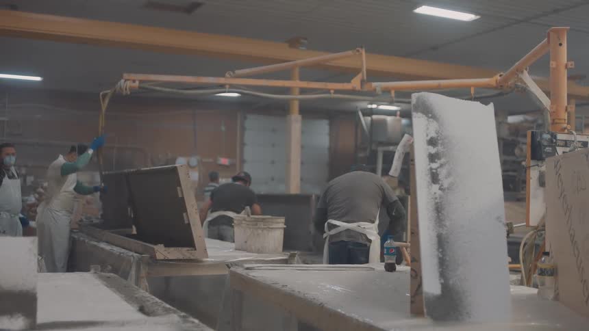 Workers handle large panels in industrial setting with cutting equipment and protective gear