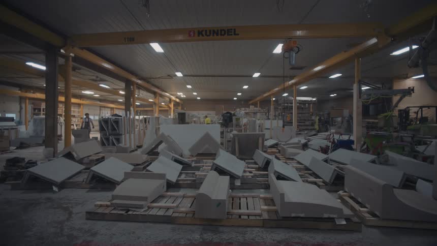 People work in a warehouse in a room with large piece of merchandise lying on wooden pallets