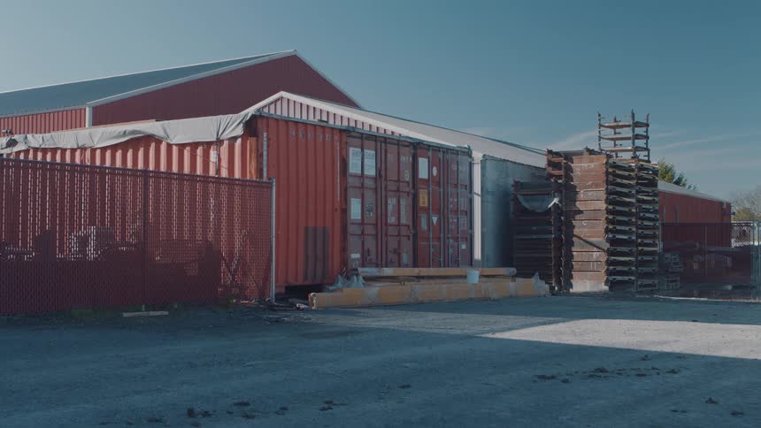 Cargo container stands beside stacked structures in an open industrial area