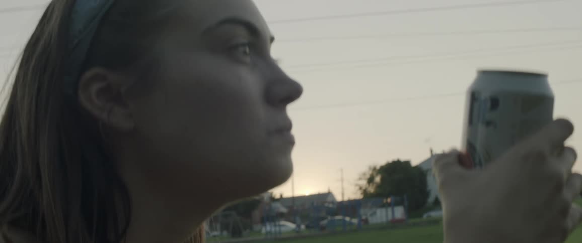 Woman drinking a can of beer outside and smiling at sunset