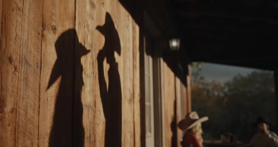 Shadows of two people wearing hats cast on a sunlit wooden wall
