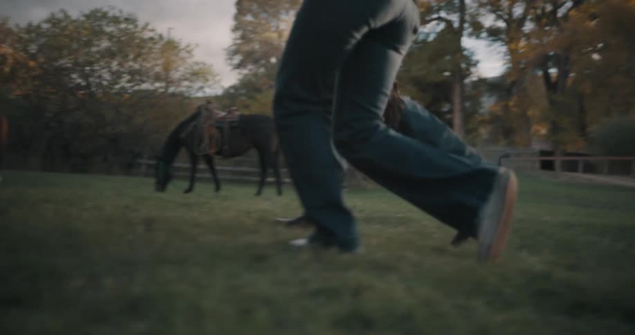 Legs of people run across grass in an open area with trees in the background