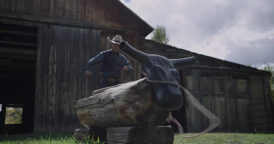 Person throws a lasso at a wooden bull head target in front of a rustic barn