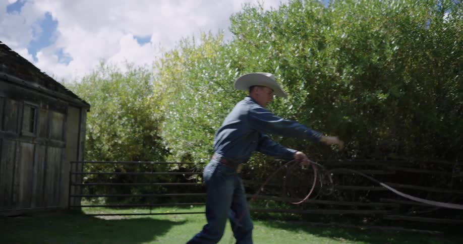 Person swings a lasso in an outdoor area surrounded by trees and a wooden fence