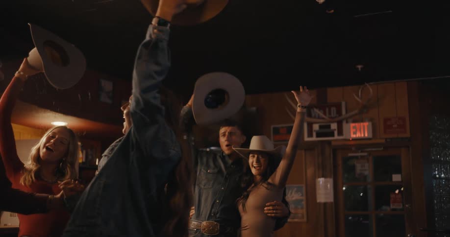Group of people celebrate in a bar raising cowboy hats and arms in the air