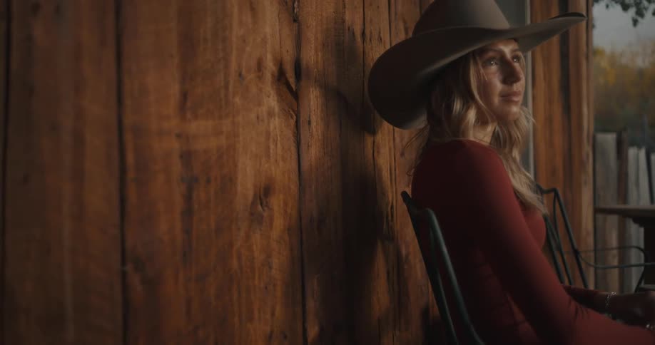 A young woman wearing a cowgirl hat sits outside on a porch