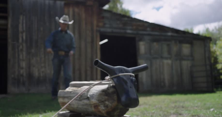 Cowboy throwing a lasso in a rural area in front of a wooden barn with a bull head target