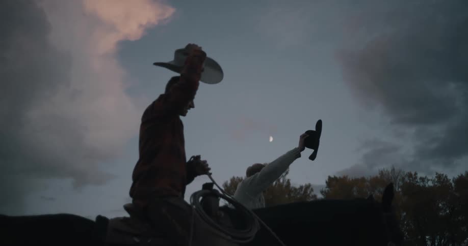 Riders on horseback raising hats under a cloudy evening sky