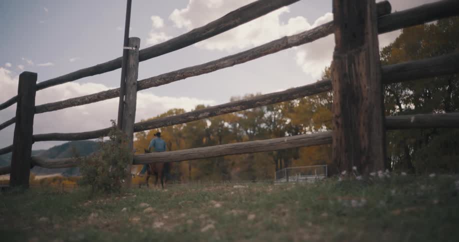 Rider on horseback moving through a fenced area with autumn trees in the background