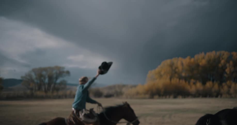 Two riders galloping across an open field with raised hats and trees in the background