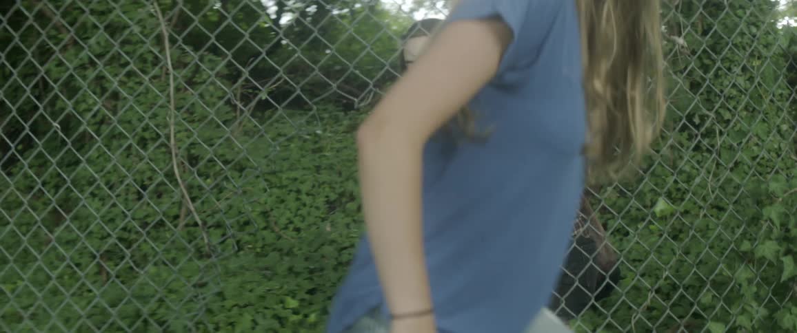 Two women climb through the hole in a chain link fence