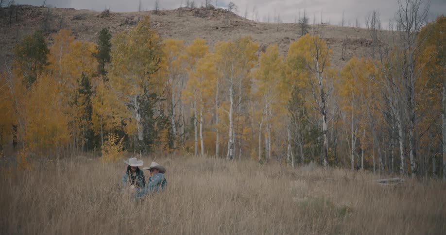 Couple in a field of tall grass with autumn trees in the background
