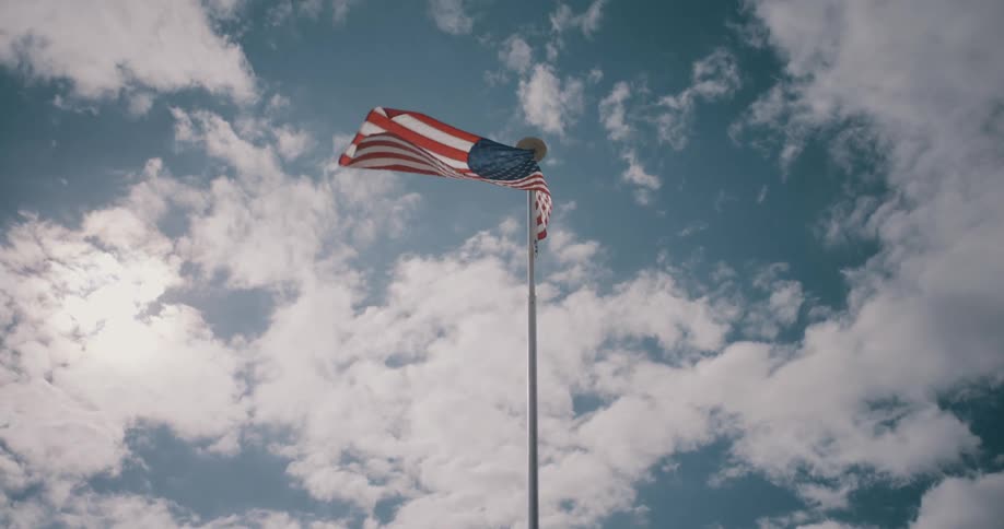 Sunlight shines on an american flag flying under a cloudy sky