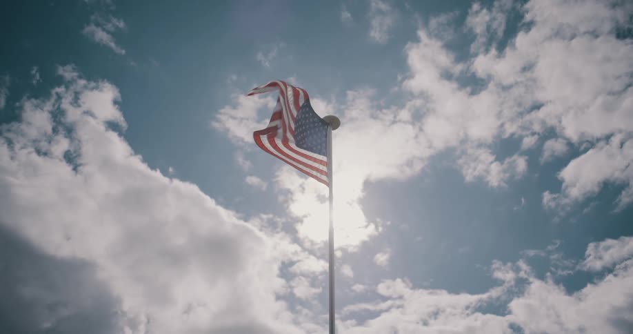 United states flag waves on a tall pole against a blue sky with scattered clouds