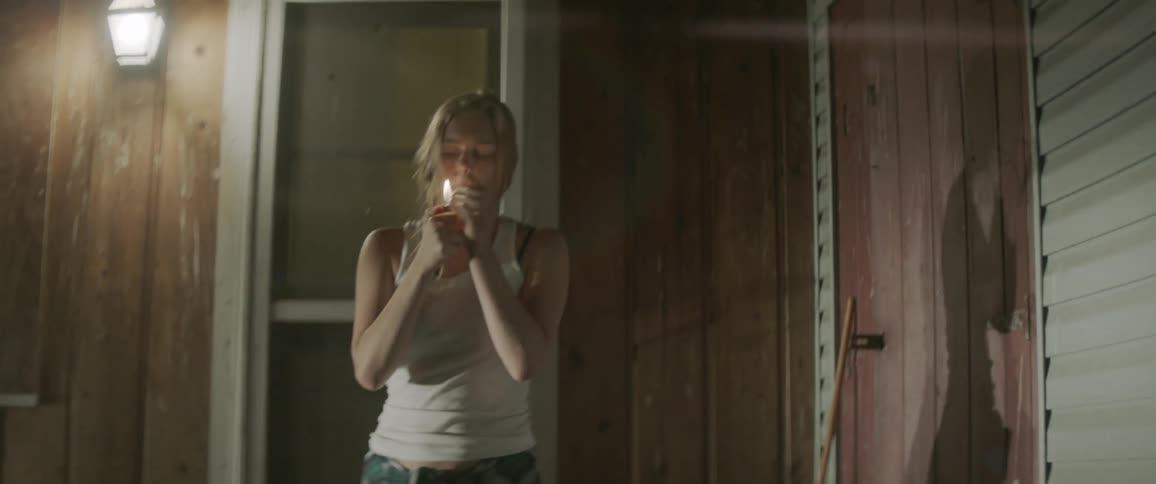 A woman walks outside at night and lights a cigarette