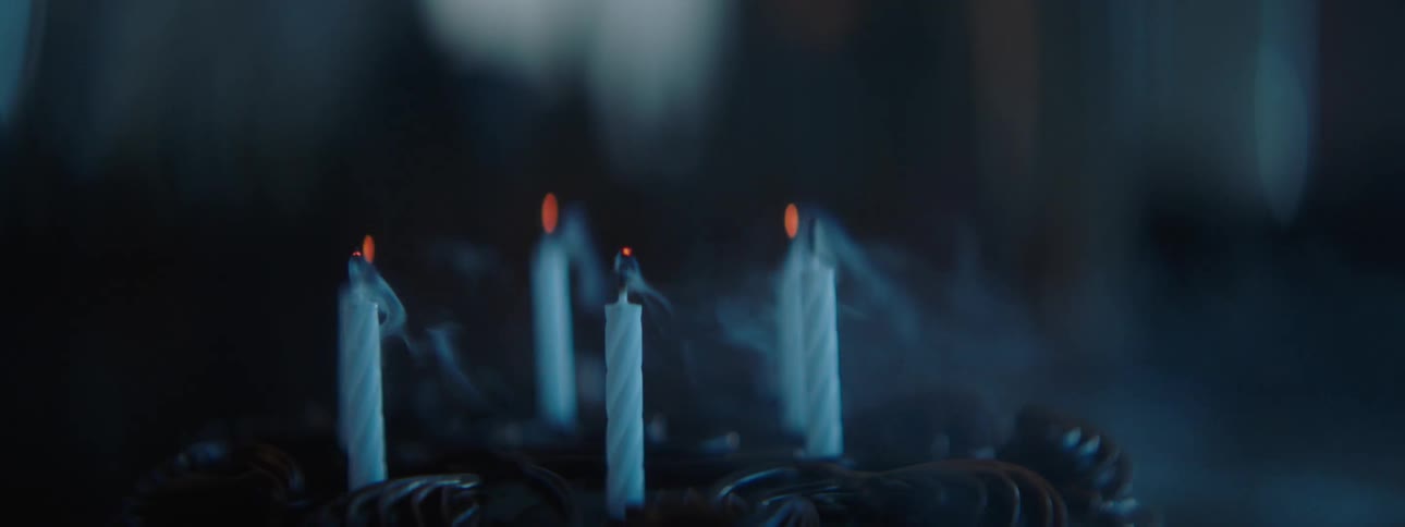 Wisps of smoke rise from the wicks of extinguished birthday candles on a chocolate cake before they magically burst back to life in a warm bright flame