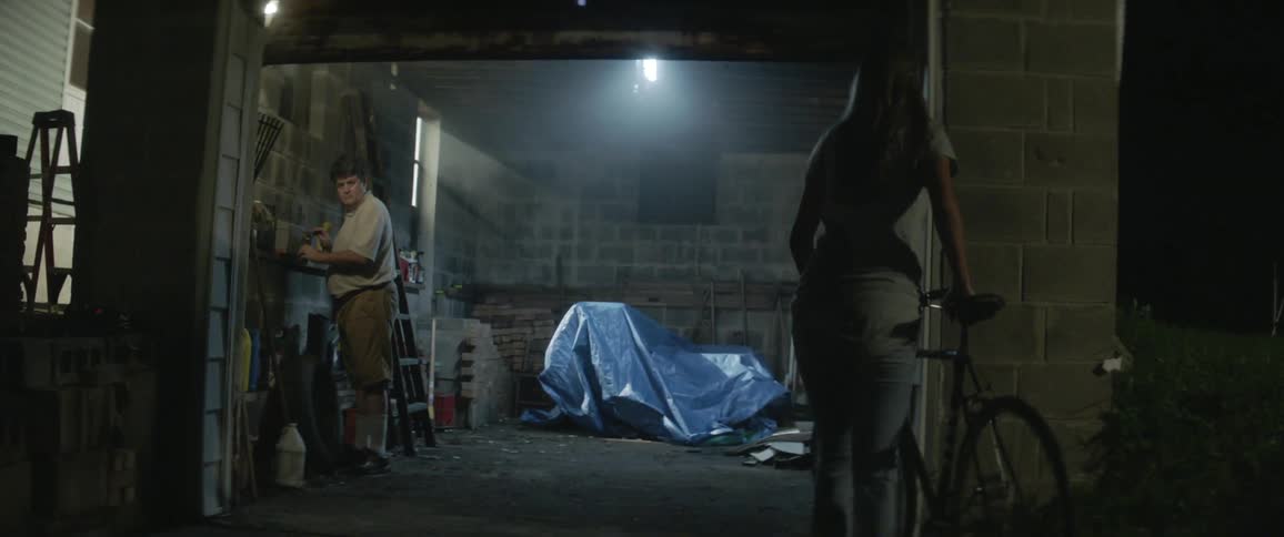 A woman carries her bike to a garage where a man is standing inside