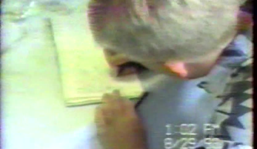 Boy writes in a book while sitting in a room with others