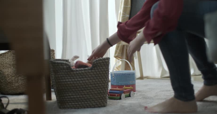 A woman picks up toys in a living room and places them in a basket