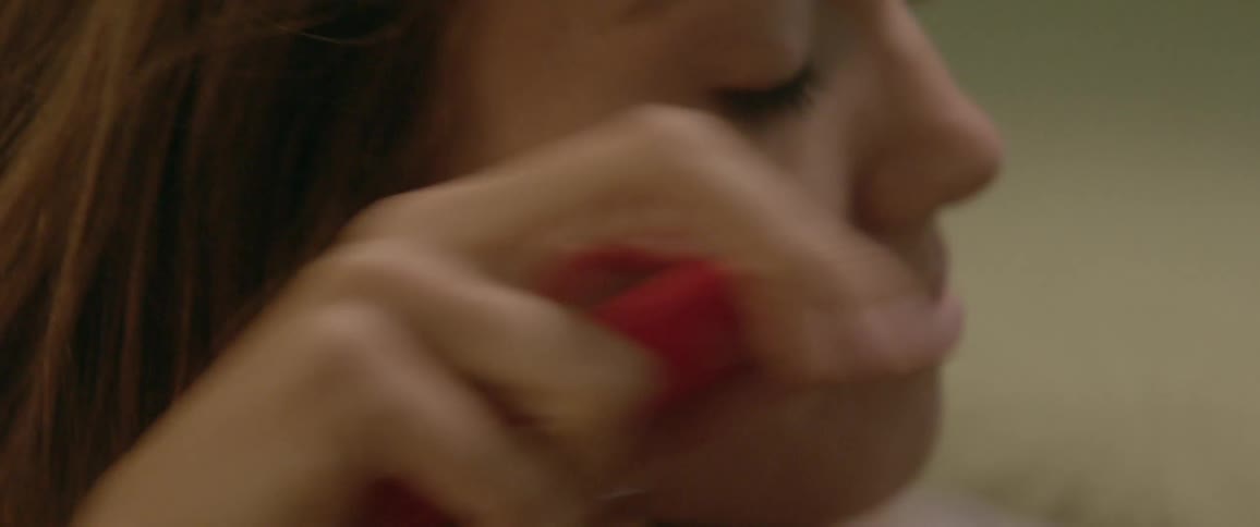 A woman holding a pen cap in her mouth and crying as she writes in a book