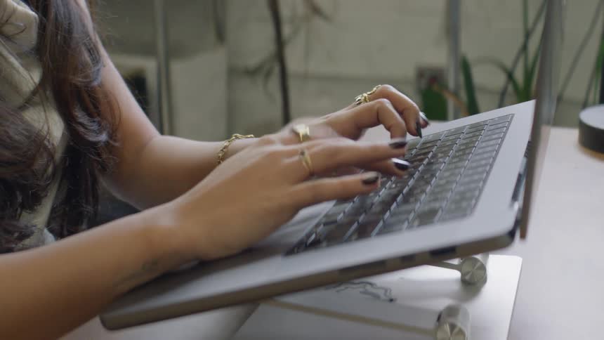 Closeup of a woman hands typing on a laptop keyboard at a desk indoors
