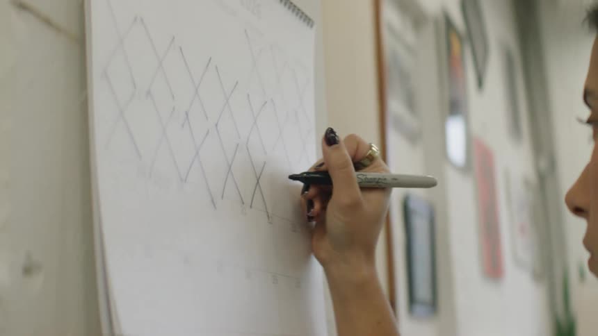 Young female person crossing dates on a calendar hanging on a wall indoors during day time