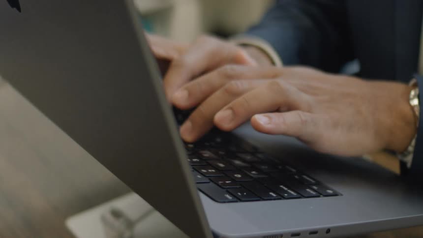 Man sitting in an office types on a laptop on a laptop stand