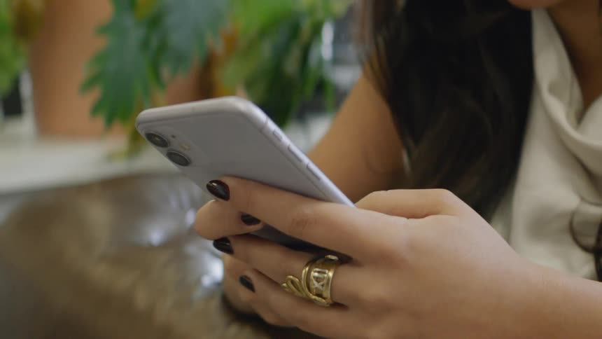 Young woman sitting down holding her phone with both hands texting with her thumbs