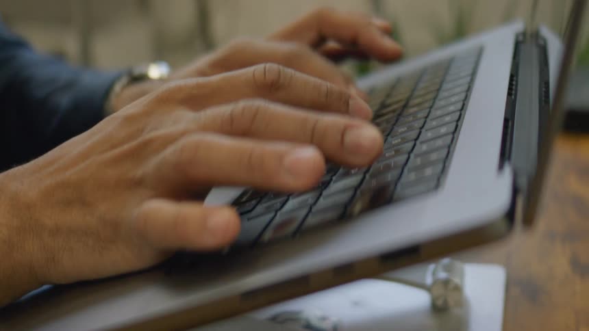 A pair of hands are typing on a laptop on a wood desk