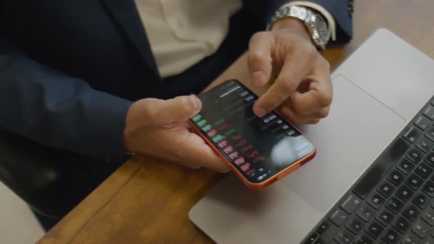 Man sitting in an office reviews stocks on an app on his smartphone