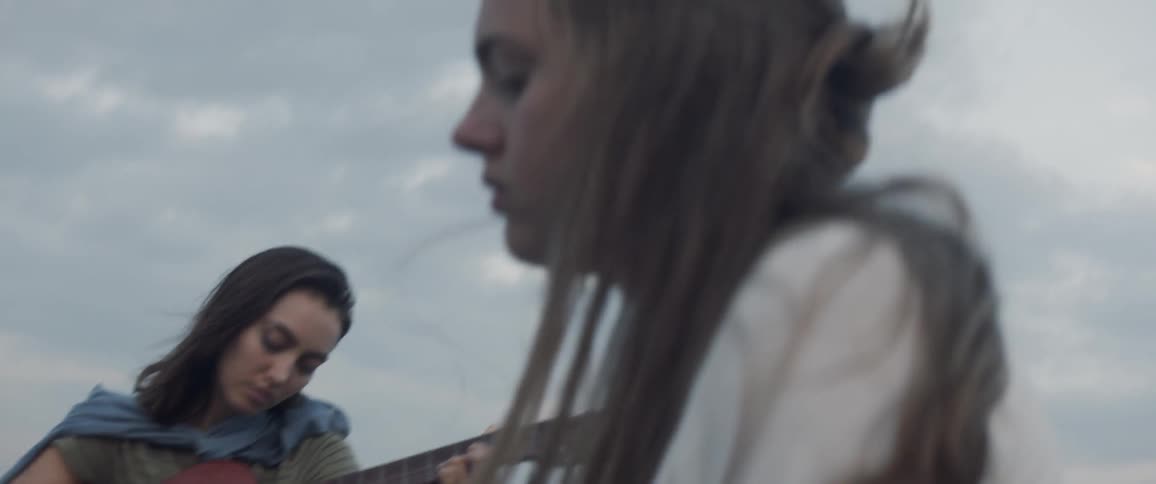 Woman playing guitar next to another woman on windy overcast day
