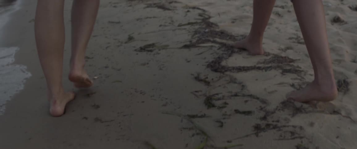 Two people walking in a beach as seen from their knees down