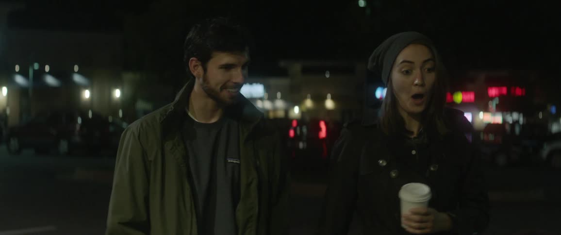 A man and woman walk outside at night talking